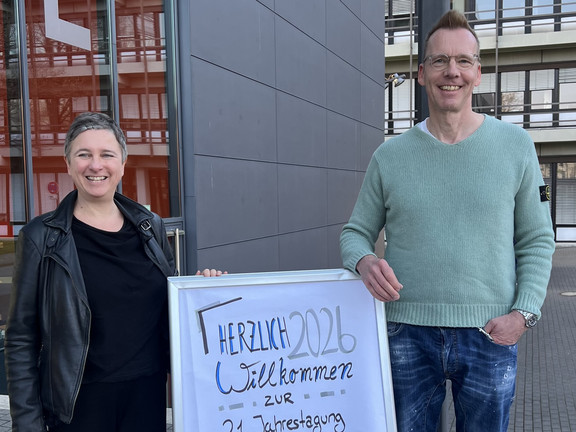 Eva Cendon (links) und Uwe Wilkesmann (rechts) stehen neben dem Plakat zur GfH.