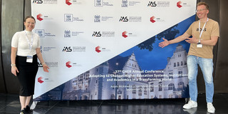 Olga Wagner (left) and Uwe Wilkesmann (right) standing in front of the Cher Conference poster..