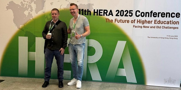 Peter Woelert (links) und Uwe Wilkesmann (rechts) vor dem Plakat der HERA Conference.