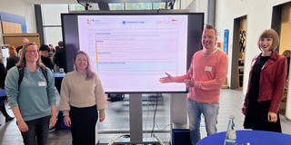 from left to right: Alina Breitzke, Olga Wagner, Uwe Wilkesmann, Viktoria Jäger in front of the screen with the programme announcement.